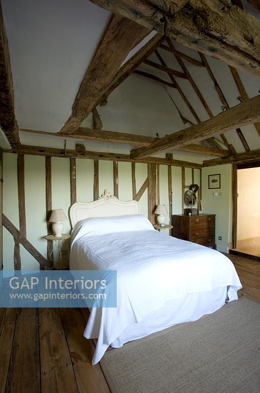 Ferme Boonshill, East Sussex. Intérieur de la chambre avec parquet, poutres apparentes et lit avec tête de lit français en bois.