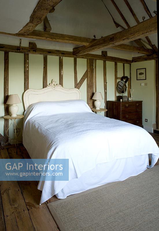 Ferme Boonshill, East Sussex. Intérieur de la chambre avec parquet, poutres apparentes, tête de lit française et vieilles tables d'appoint en métal.