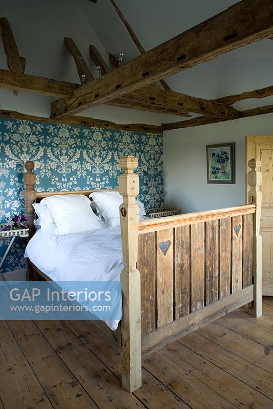Ferme Boonshill, East Sussex. Intérieur de la chambre à coucher avec lit en bois récupéré par mick shaw de vieil escalier et parquet. papier peint bleu paon décore le mur.