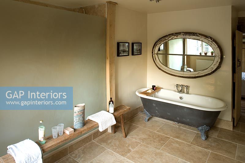 Ferme Boonshill, East Sussex. Intérieur de salle de bain avec baignoire sur pieds, banc en bois d'Inde et miroir fabriqué à partir d'une vieille fenêtre.