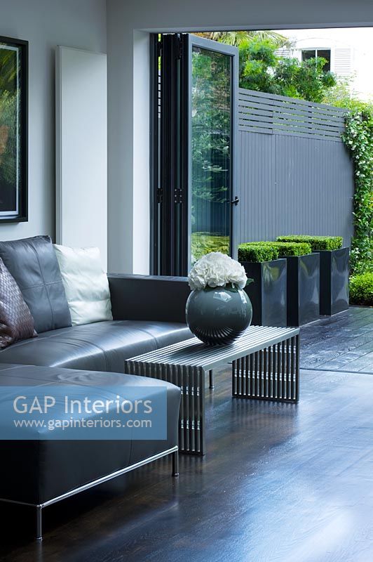 Salon contemporain avec canapé d'angle en cuir gris, vase et table basse, donnant sur le patio et le jardin conçu par Charlotte Rowe