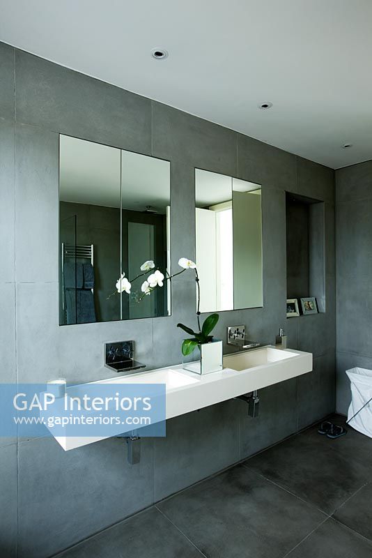 Salle de bain contemporaine élégante avec double évier mural en pierre, murs en ardoise grise, miroirs et orchidée blanche