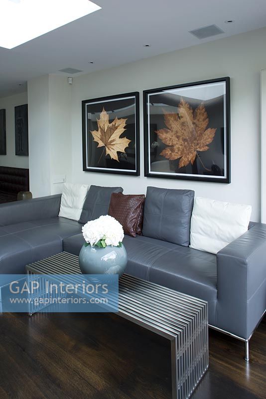 Salon contemporain avec canapé en cuir gris, table basse en métal avec vase moderne et imprimés de feuilles sur le mur