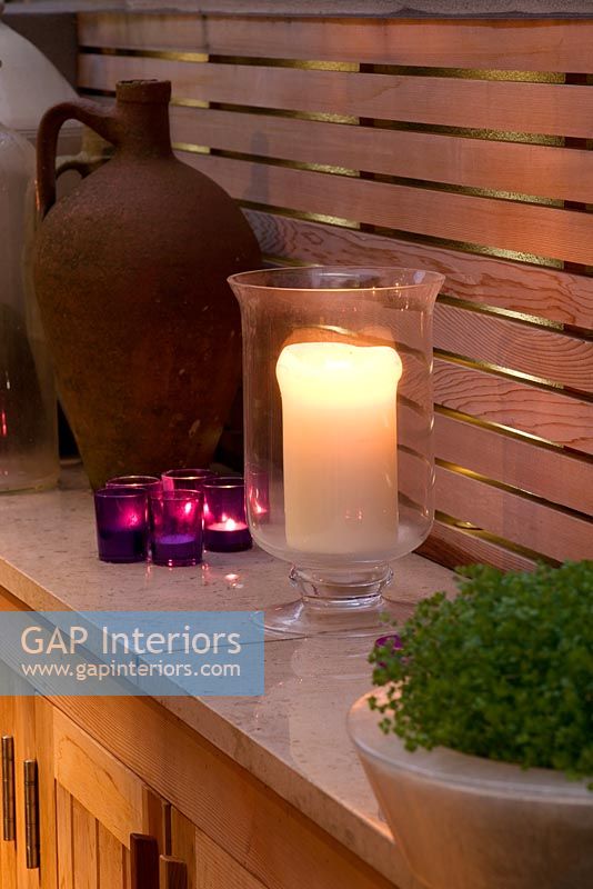 Jardin de nuit avec bougies sur étagère en marbre, ancienne urne en terre cuite et treillis en bois