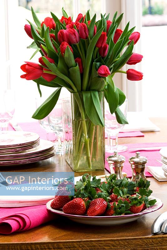 Tulipes rouges dans un vase et assiette de fraises sur table à manger