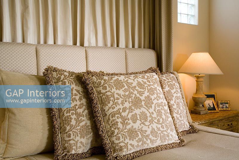 Détail d'oreillers décoratifs aux tons neutres sur lit avec lampe.