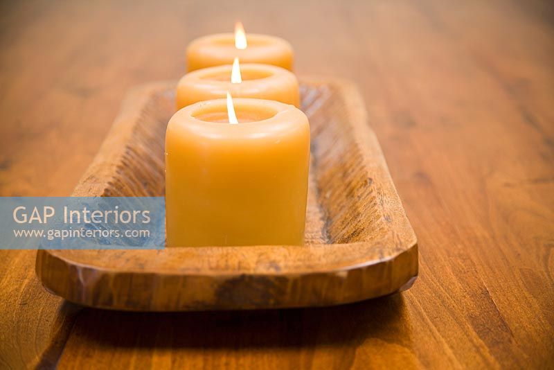 Détail de trois bougies allumées sur support en bois.