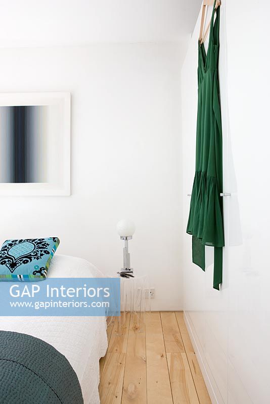 Chambre avec coussin à motifs turquoise et robe verte accrochée au mur