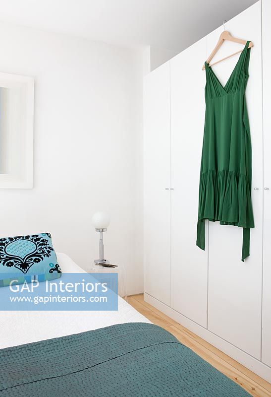Chambre avec coussin à motifs turquoise et robe verte suspendue à l'armoire