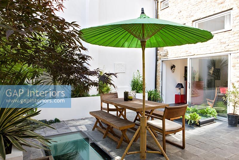 Petit jardin urbain avec mobilier en bois et parasol vert