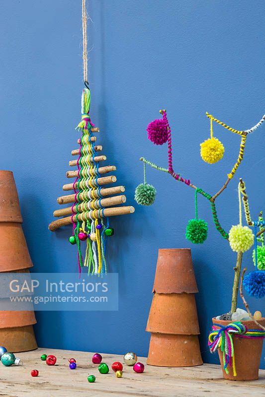 Un arbre de Noël coloré fait de bâtons, de laine colorée et de boules miniatures sur fond bleu