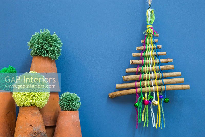 Un arbre de Noël coloré fait de bâtons, de laine colorée et de boules miniatures sur fond bleu