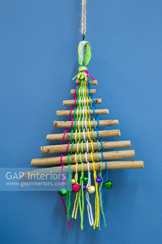 Un arbre de Noël coloré fait avec des bâtons de laine colorée et des boules miniatures sur un fond bleu
