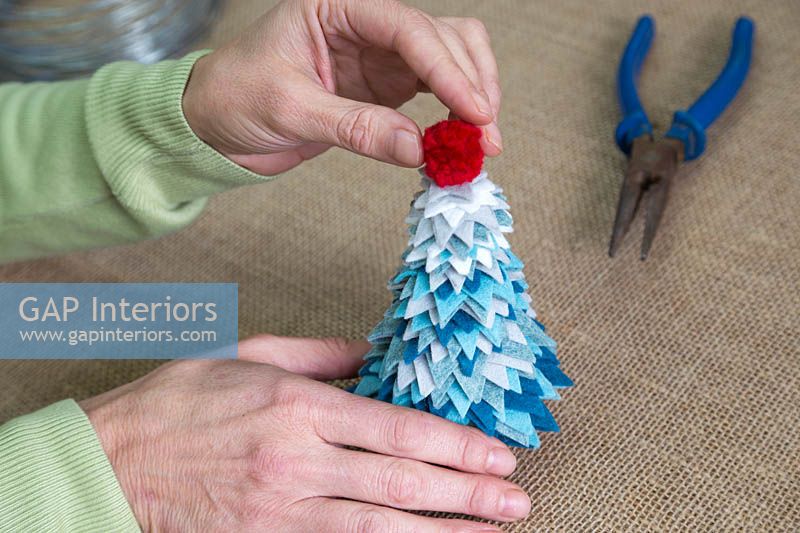 Faire un sapin de Noël en feutre - Ajoutez le pompon au sommet de l'arbre pour le finir