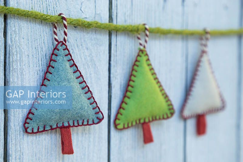 Fabrication de décorations de Noël en feutre cousu - arbres de Noël miniatures en feutre et chaîne décorative, suspendus contre un panneau en bois