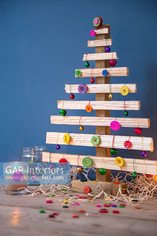 Un sapin de Noël en bois décoré de boutons et de boules de couleur