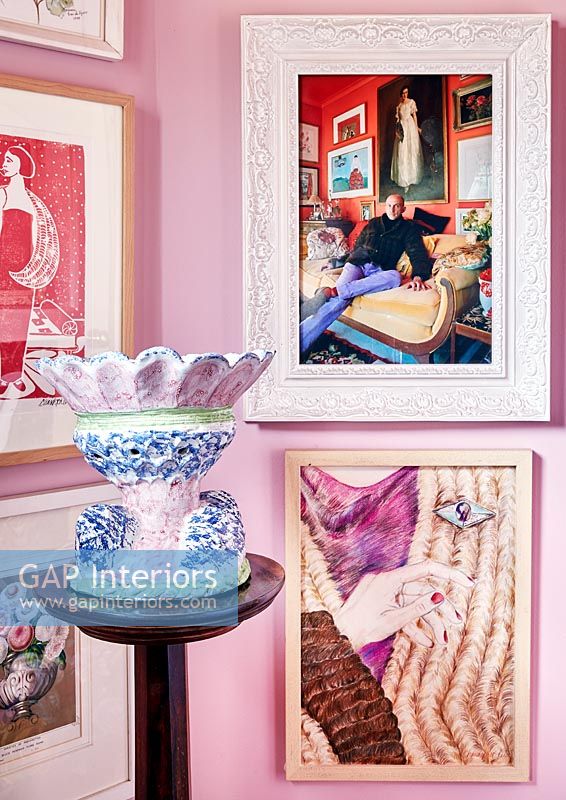 Photographies et peintures encadrées sur un mur rose avec des poteries colorées