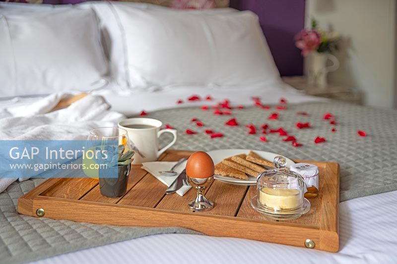 Plateau de petit déjeuner et peignoir avec des pétales de rose sur le lit