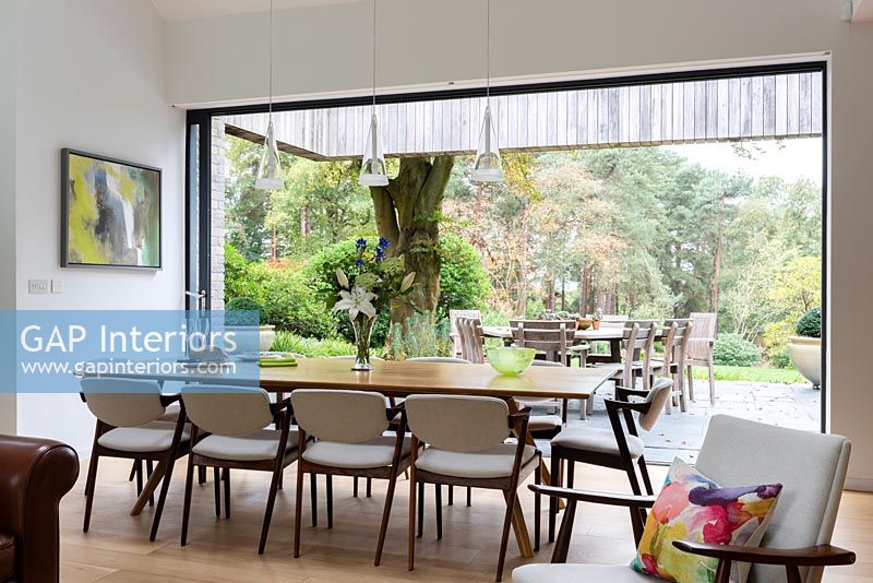 Grande table à manger par des portes-fenêtres ouvertes avec vue sur les jardins boisés