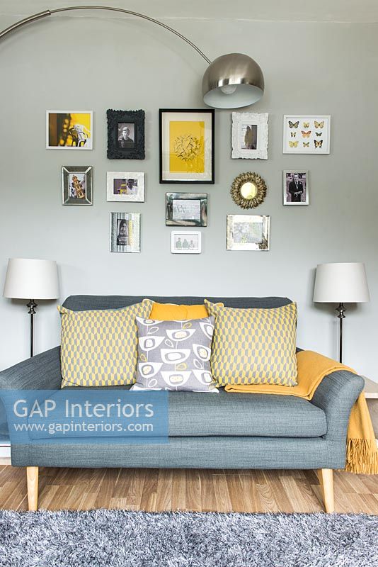 Canapé gris avec coussins jaunes et affichage d'images sur mur peint gris