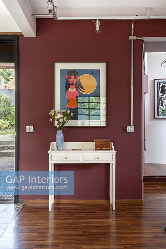 Table console blanche et illustrations colorées sur mur peint en rouge foncé