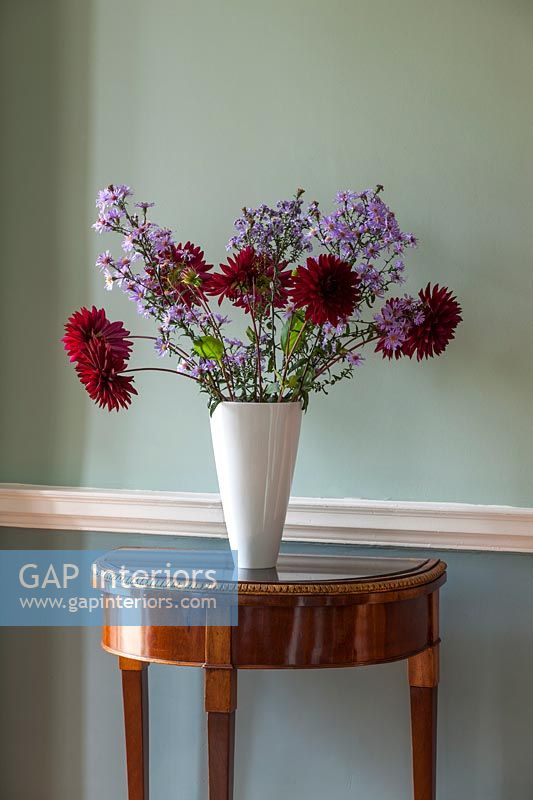 Fleurs rouges et violettes dans un vase blanc sur une table console antique