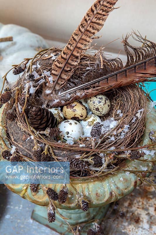 Urne vintage en métal avec nid d'oiseaux, plumes et œufs comme décoration