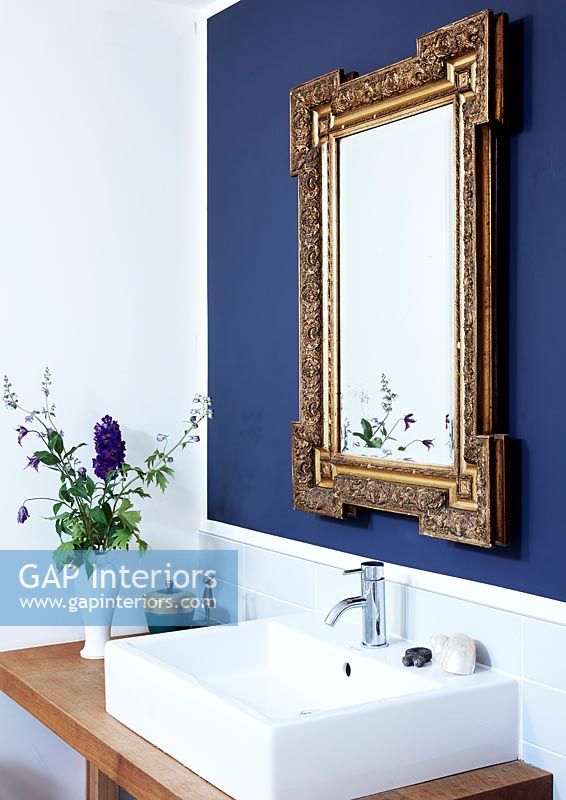 Miroir doré sur mur bleu foncé au-dessus du lavabo de la salle de bain