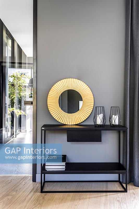 Table console avec miroir circulaire doré contre mur peint gris
