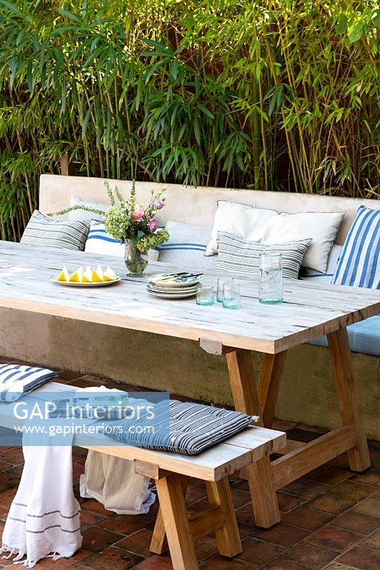 Table à manger d'extérieur en bois avec banquette intégrée recouverte de coussins