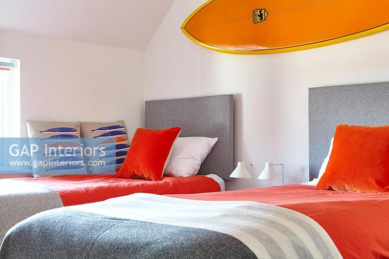 Planche de surf orange vif au-dessus de lits jumeaux dans une chambre moderne