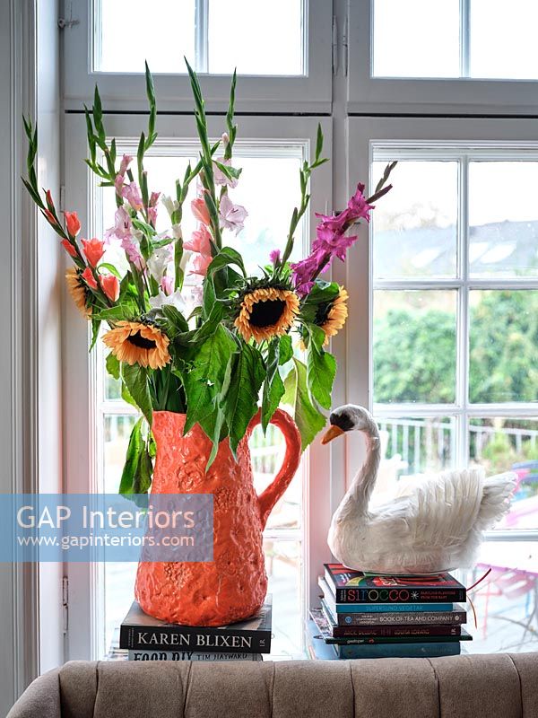 Vase cruche orange vif plein de fleurs sur le rebord de la fenêtre