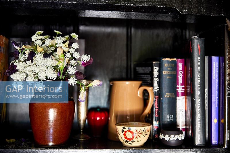 Fleurs en pot en céramique à côté de livres et ornements sur étagère noire