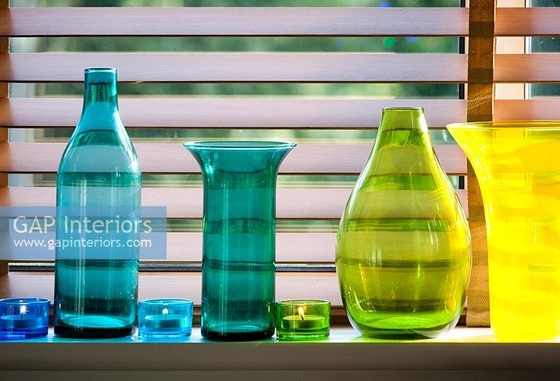 Collection de verrerie colorée sur le rebord de la fenêtre avec des bougies chauffe-plat