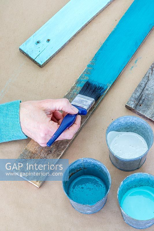 Femme peint une planche en bois rustique dans différents tons de turquoise à l'aide d'un pinceau
