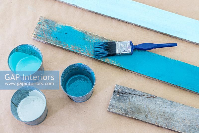 Planches de bois rustiques peintes dans divers tons de turquoise, y compris pinceau et pots de peinture