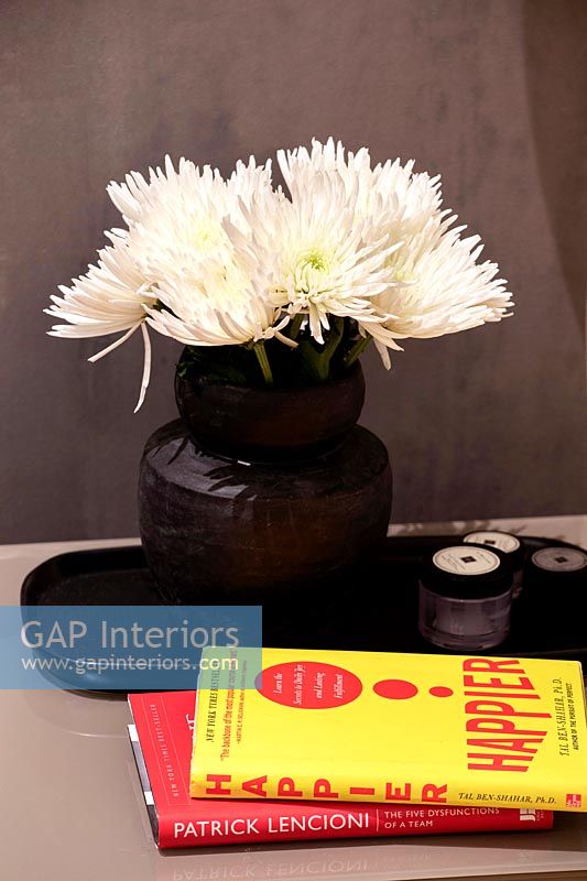 Vase noir avec des fleurs coupées blanches sur la table de chevet avec du matériel de lecture