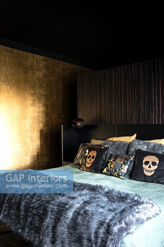 Chambre noire et or avec jet de fourrure et coussins à motifs de crâne sur le lit