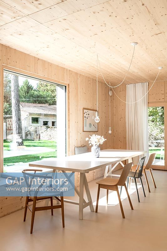 Salle à manger moderne dans une maison en bois avec grande baie vitrée avec vue sur jardin