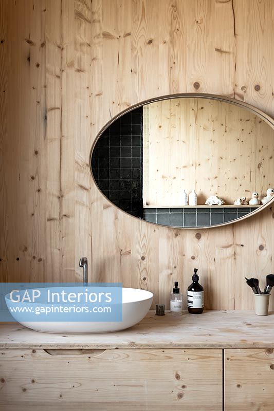 Grand miroir ovale au-dessus du lavabo dans la salle de bains en bois