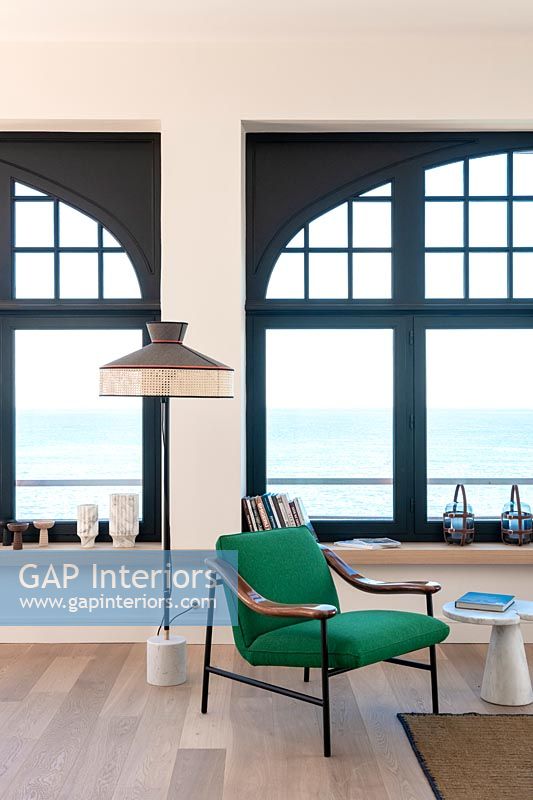 Fauteuil vert et lampadaire vintage à côté de grandes fenêtres avec vue sur la mer
