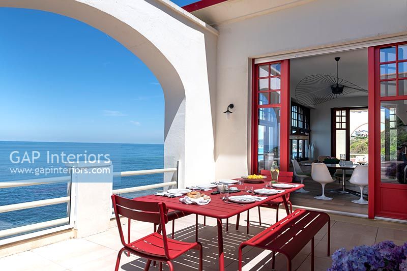Table à manger rouge sur terrasse blanche avec vue sur la mer