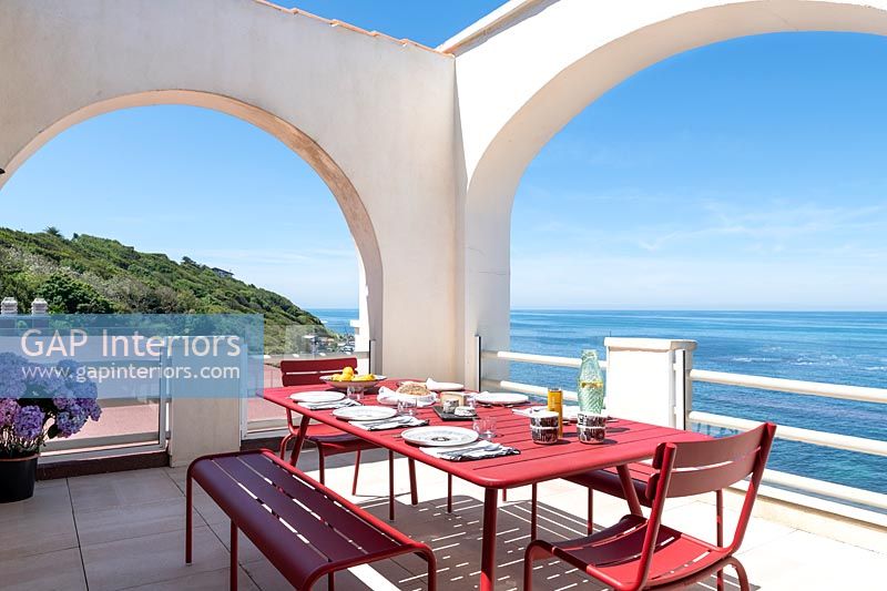 Table à manger rouge dressée pour le déjeuner sur la terrasse avec vue sur la mer en été