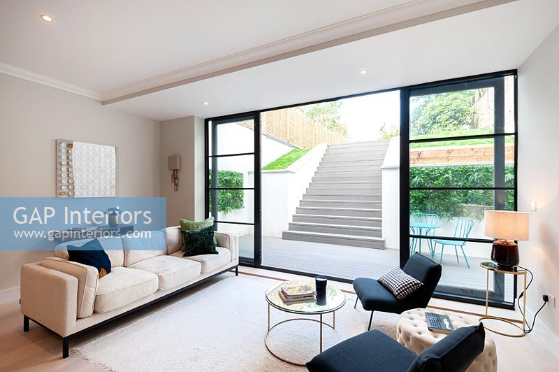 Salon monochrome moderne avec vue à travers des portes-fenêtres ouvertes sur une terrasse en contrebas