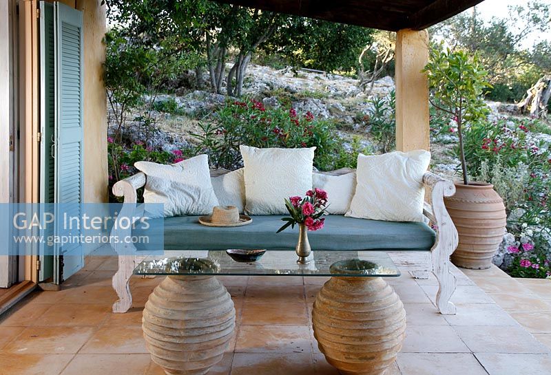 Canapé en bois orné sur terrasse couverte avec table en verre et urne en argile