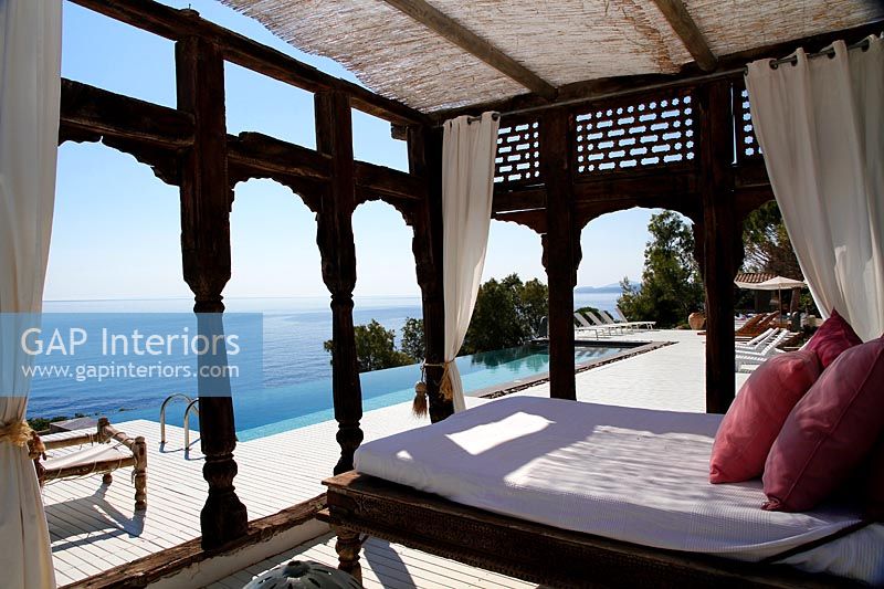 Pergola décorative avec grand lit sur terrasse extérieure avec piscine et vue mer
