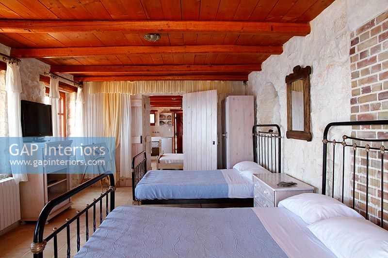 Deux lits doubles dans une chambre de campagne avec poutres apparentes et murs en briques