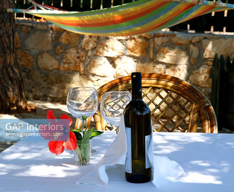 Nappe et bouteille de vin sur petite table de jardin ombragée par des arbres avec hamac