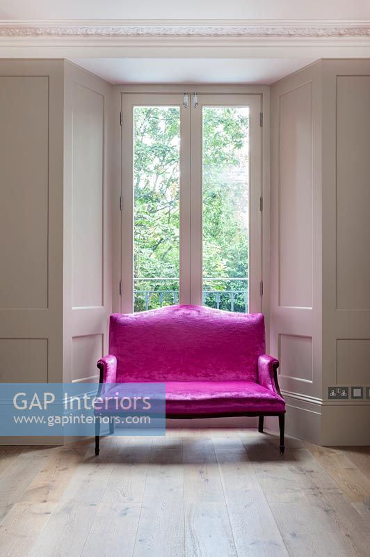 Canapé rose vif à côté de la fenêtre dans le salon lambrissé