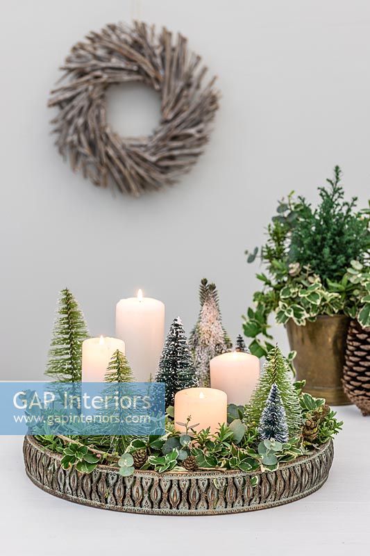 Arrangement de l'Avent avec plateau en métal orné, bougies blanches, feuillage panaché d'Euonymus, eucalyptus et faux sapins de Noël miniatures